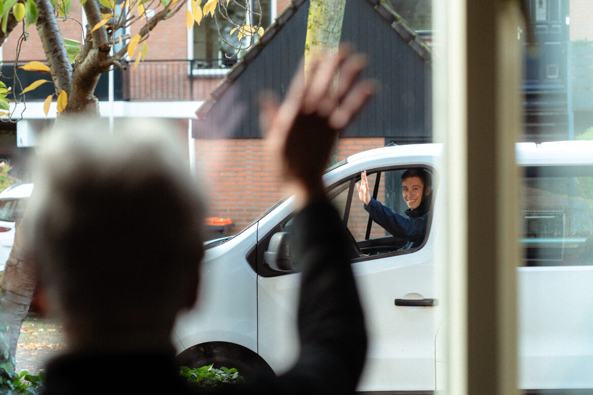 Man zwaait uit een busje naar oudere vrouw