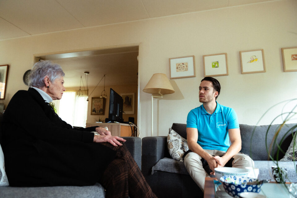 Jonge man in gesprek met oudere vrouw in de woonkamer