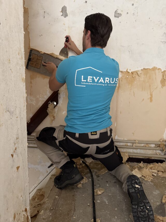 Een medewerker van Levarus verwijdert behang van een muur tijdens een ontruiming, als onderdeel van de aanvullende diensten die het bedrijf aanbiedt om een woning opleverklaar te maken.