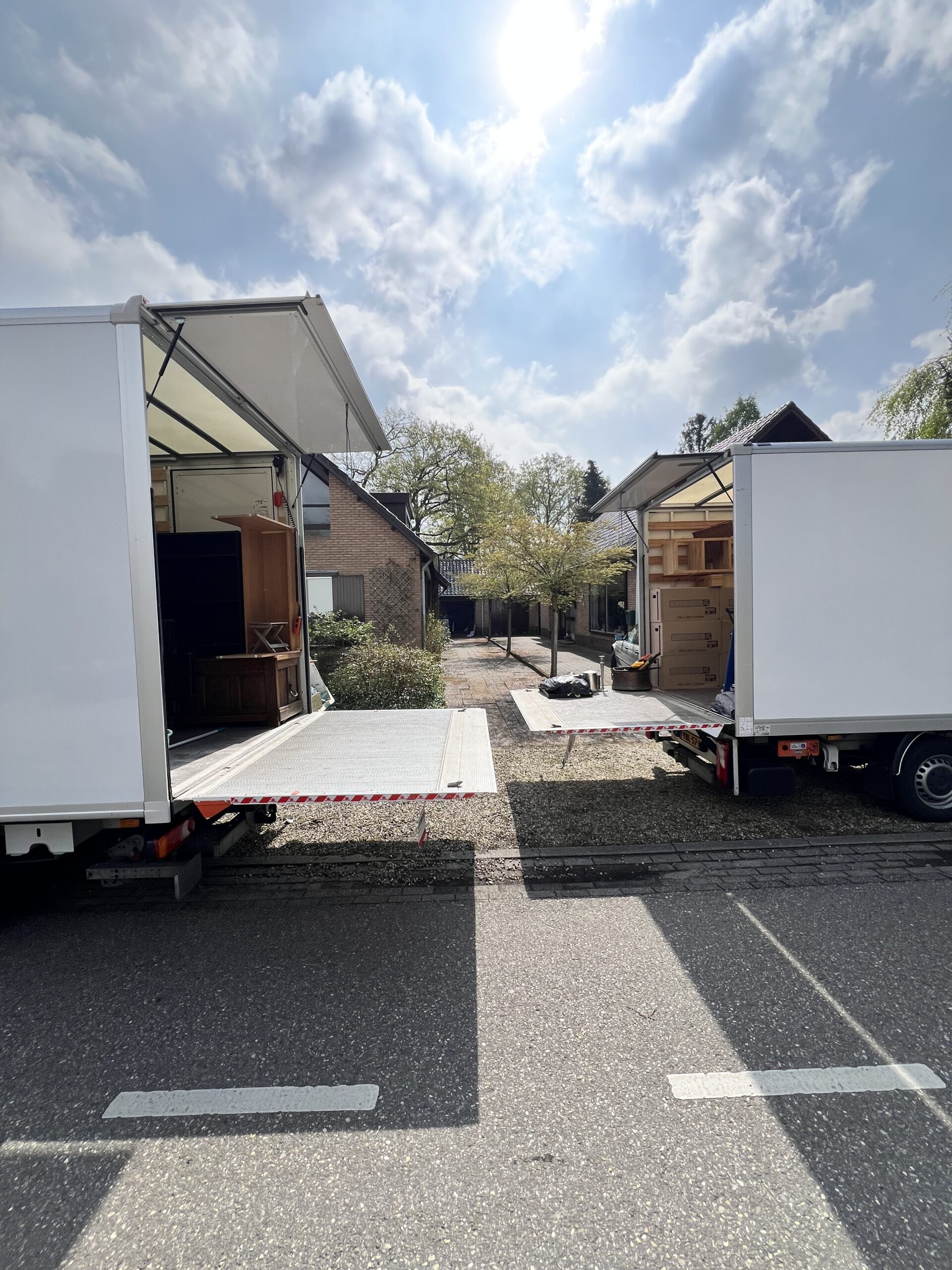 Levarus voert een woningontruiming uit met twee verhuiswagens in een rustige woonwijk, zonnige dag